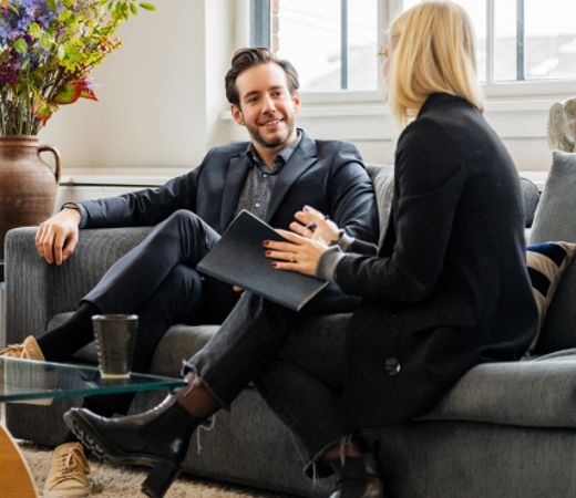 Two 7N employees talking while sitting on a grey sofa in the office